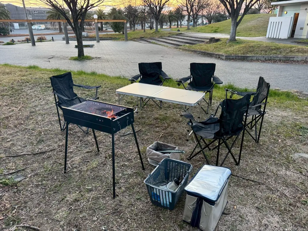 芝生に設営したバーベキュー一式。炭に火が入ったコンロ、テーブル、椅子、クーラーボックス。